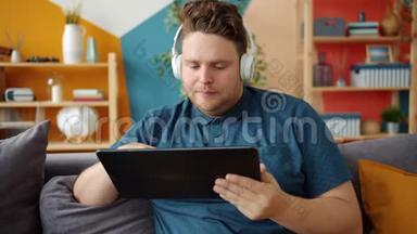 戴着耳机的严肃男人在家里用平板电脑触摸电子屏幕